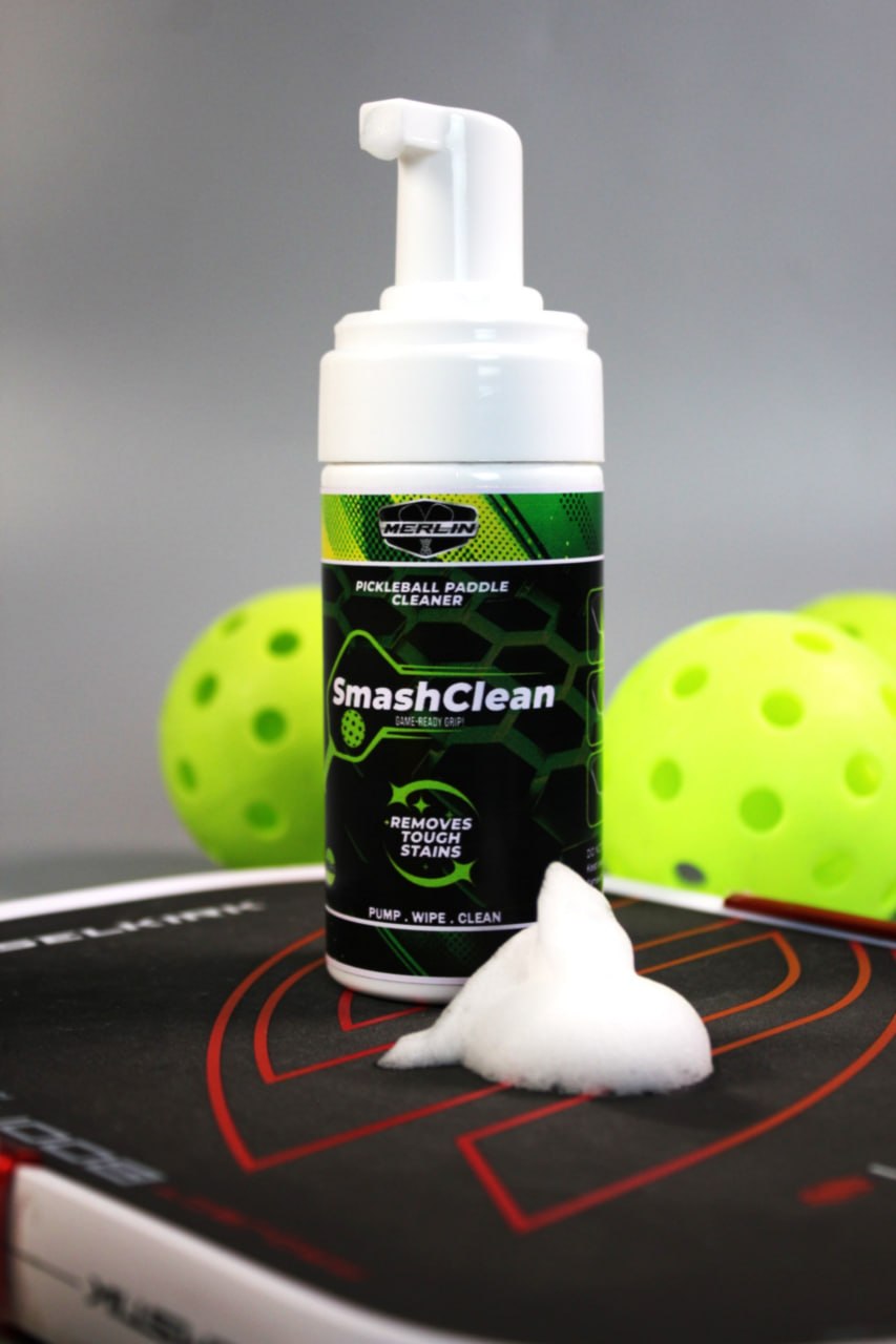 A bottle of SmashClean standing on a pickleball paddle, with a dollop of white foam on the paddle face